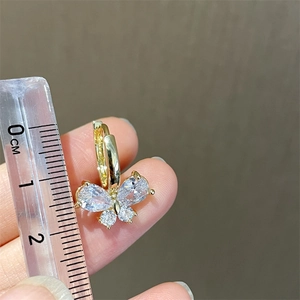 Macro detail of gold butterfly earrings with zircon stones next to a size scale ruler