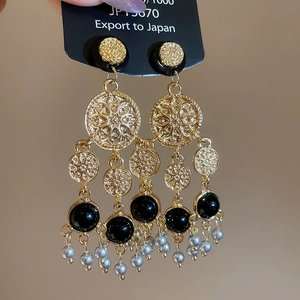 Détail d'une boucle d'oreille vintage dorée avec cabochon noir et perle grise pendante