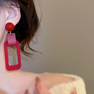 Detail of red geometric leather-textured earring worn by model against a soft wall