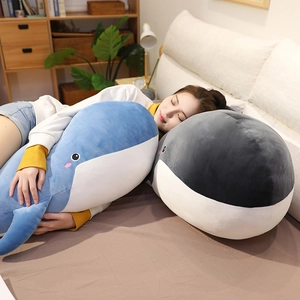 A girl resting on large blue and grey whale plush toy pillows in a cozy bedroom