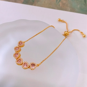 Gros plan d'un bracelet coeur plaqué or avec zircons roses et sertissage micro-pavé