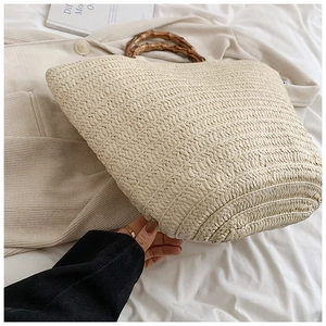 Detailed view of handmade straw tote bag featuring natural bamboo handles on woven fabric