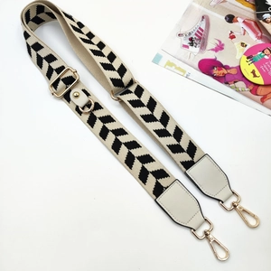 Dettaglio della tracolla regolabile in tela beige e nera con ganci in metallo dorato