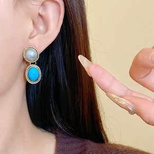 Detail of vintage gold earrings with white pearl and oval turquoise resin stones