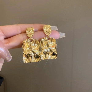 Gros plan de boucles d'oreilles vintage dorées avec texture froissée tenues à la main
