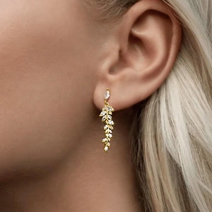 Detail of elegant gold-toned leaf tassel earrings with sparkling zircon gemstones