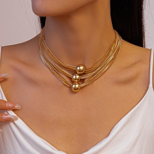 Detail of layered gold chain necklace featuring three polished metallic beads on the collar