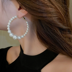 Close-up of model wearing oversized gold hoop earrings with gradient white pearls