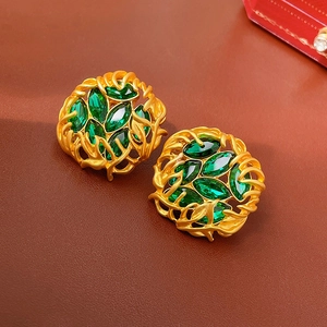 Détail de boucles d'oreilles vintage dorées avec pierres vert émeraude sur cuir marron