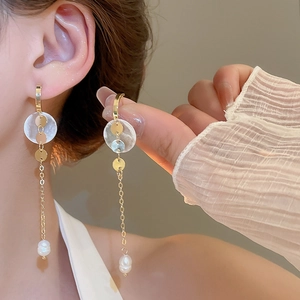 Detail of long gold chain earrings with shell discs and pearl drops on a model
