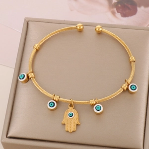 Detail of 18K gold-plated twisted bangle featuring Hamsa hand and blue Evil Eye charms