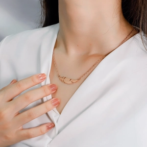 Close-up of elegant rose gold feather pendant necklace on a minimalist white shirt background