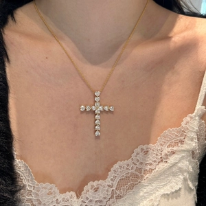 Close-up of gold cross pendant necklace with heart-cut crystals on a lace collar
