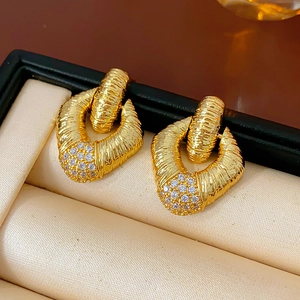 Macro detail of golden diamond-patterned earrings with clear crystals in a jewelry box