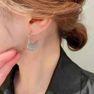 Detailed shot of silver C-shaped tassel earrings on model showing a metallic teardrop design