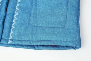 Makroaufnahme der blauen Baumwolljacke mit weißer Wellenstickerei und Taschendetails