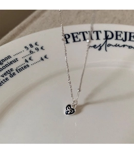Detailed view of silver bead chain necklace with black heart and bow pendant on porcelain