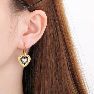 Close-up of gold heart earrings with black enamel and sparkling zircon on ear