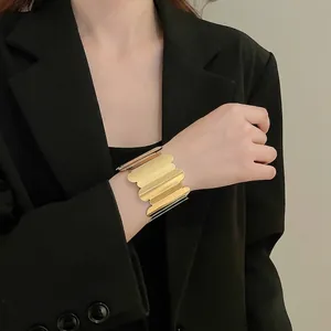 Wide gold metal open cuff bracelet with scalloped edges on model wearing black suit