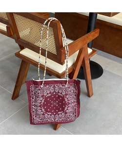 Detail of burgundy paisley tote bag with colorful beaded shoulder strap on wooden chair