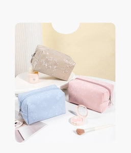 Detailed macro view of embossed floral patterns and M-letter zipper on pastel cosmetic bags