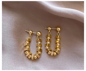 Detail of gold U-shaped earrings with geometric beads on soft silk fabric background