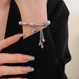 Detail of gray pearl bracelet with silver cat charm and tassel fringe on a wrist