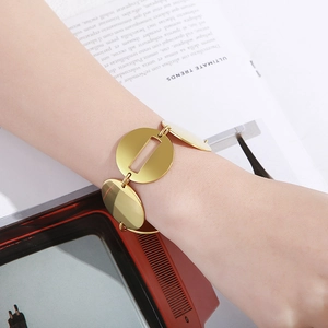 Dettaglio di un bracciale in metallo dorato con dischi tondi lucidi sul polso di una donna