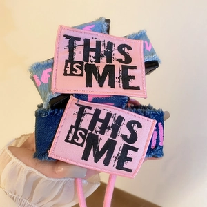 Detail of denim bow hair claw clip featuring pink graffiti and This Is Me embroidery patch