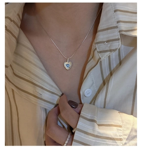 Detail view of heart-shaped silver necklace with blue gemstone on a fashion model