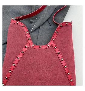 Detail of red suede tote bag featuring metallic studs and smooth leather trim finish