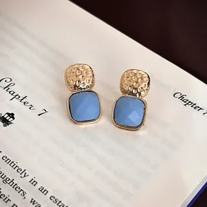 Elegant gold-tone square blue studs on vintage book pages for a minimalist look