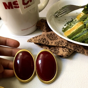 Retro oval stud earrings with burgundy center and gold border in a lifestyle setting