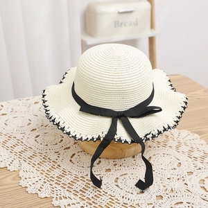 Detail of child straw hat with black bow and scalloped wave edges on wooden stand