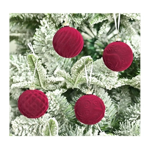 Close-up of four red velvet Christmas balls with embossed patterns on snow-covered branches
