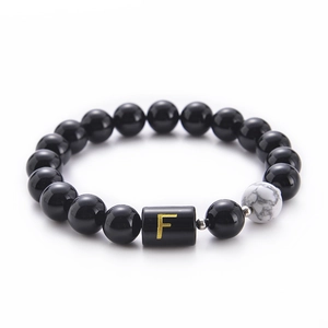Detail of 10mm black onyx and white turquoise beads with a golden letter F charm