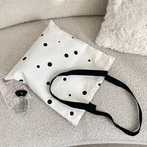 Flat lay of a white canvas tote bag with black polka dots and items on a grey fabric