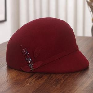 Close-up of wine red wool felt cap with beaded feathers and vintage bronze flower