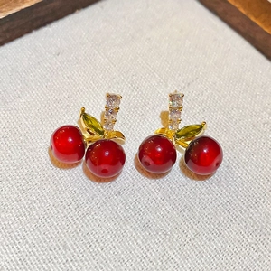 Détail des boucles d'oreilles cerises avec sphères en résine rouge et gemmes vertes