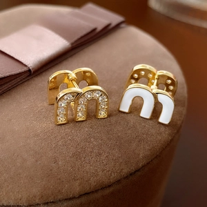 Elegant gold M-shaped earrings with white enamel and sparkling zircon on velvet box