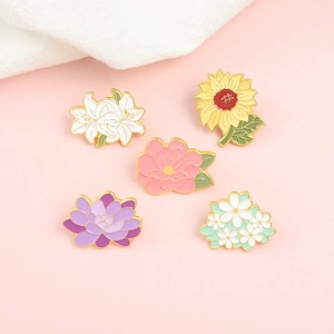 Set of five colorful enamel flower pins including sunflower and lily on pink background