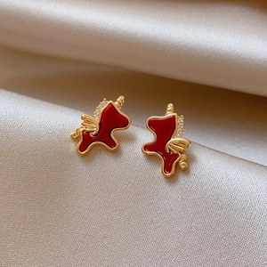 Close-up of red zircon unicorn stud earrings with gold trim on champagne silk fabric