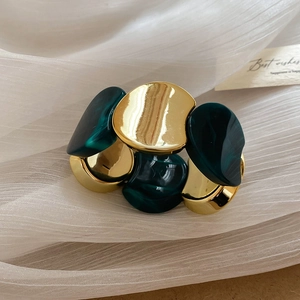 Détail d'un bracelet en résine dorée avec texture marbre vert sur fond de tissu blanc