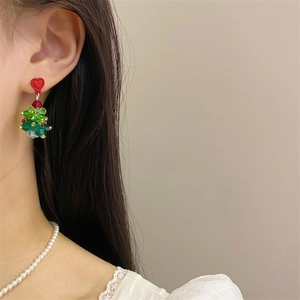 Detail of beaded Christmas tree earrings with a red bow on model's ear