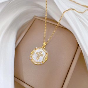 Detailed view of an octagonal gold necklace pendant with pearl and cross inlay