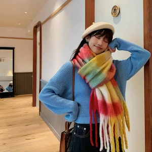 Colorful plaid tassel scarf paired with a blue knit sweater in a cozy indoor street style