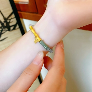 Close-up of bamboo-style gold bracelet with green jade beads and a leaf pendant on wrist