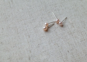 Macro detail of natural pink imitation pearl studs on textured linen background