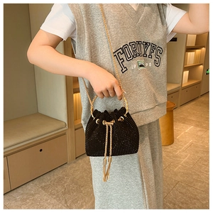 Detail of black rhinestone bucket bag with gold chain strap shown on model shoulder