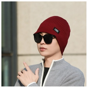 Close-up of wine red ribbed knit beanie with a black fabric label on outdoor background